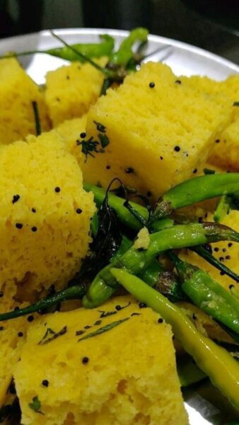 "A plate of savory dhokla garnished with mustard seeds and curry leaves."