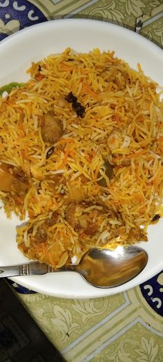 "A plate of colorful biryani garnished with fresh herbs and served with raita and lemon wedges."